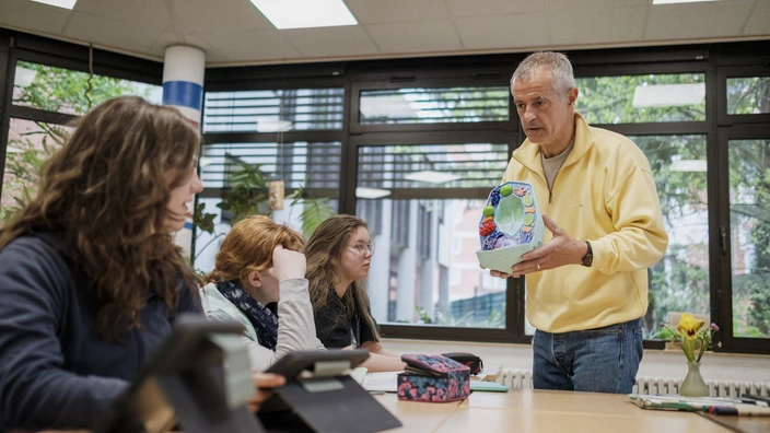 Lehrer vermittelt Schülerinnen Infos anhand eines Modell
