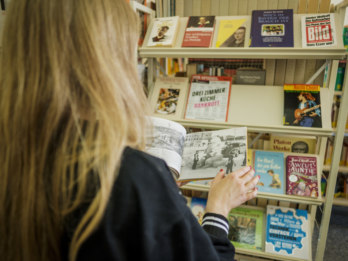 Schülerin blättert in einem Buch in der Bibliothek