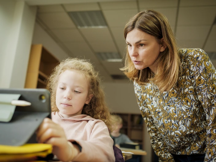 Lehrerin schaut Schülerin mit iPad über die Schulter